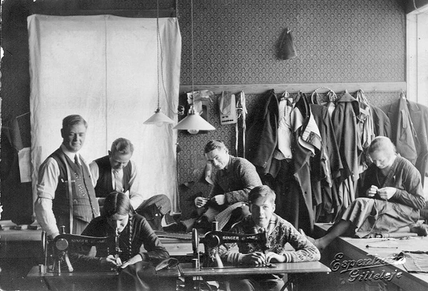 Skrædder H.P. Sørensens skrædderværksted. Billedet er fra foråret 1934. Fra venstre H.P. Sørensen, bagest fra venstre skræddersvend Henry Hansen, skræddersvend Erik Svendsen og syerske Ely Elisabeth Korneliussen. Ved symaskinerne Anna Nielsen og Poul Jørgensen, H. P. Sørensens søn.