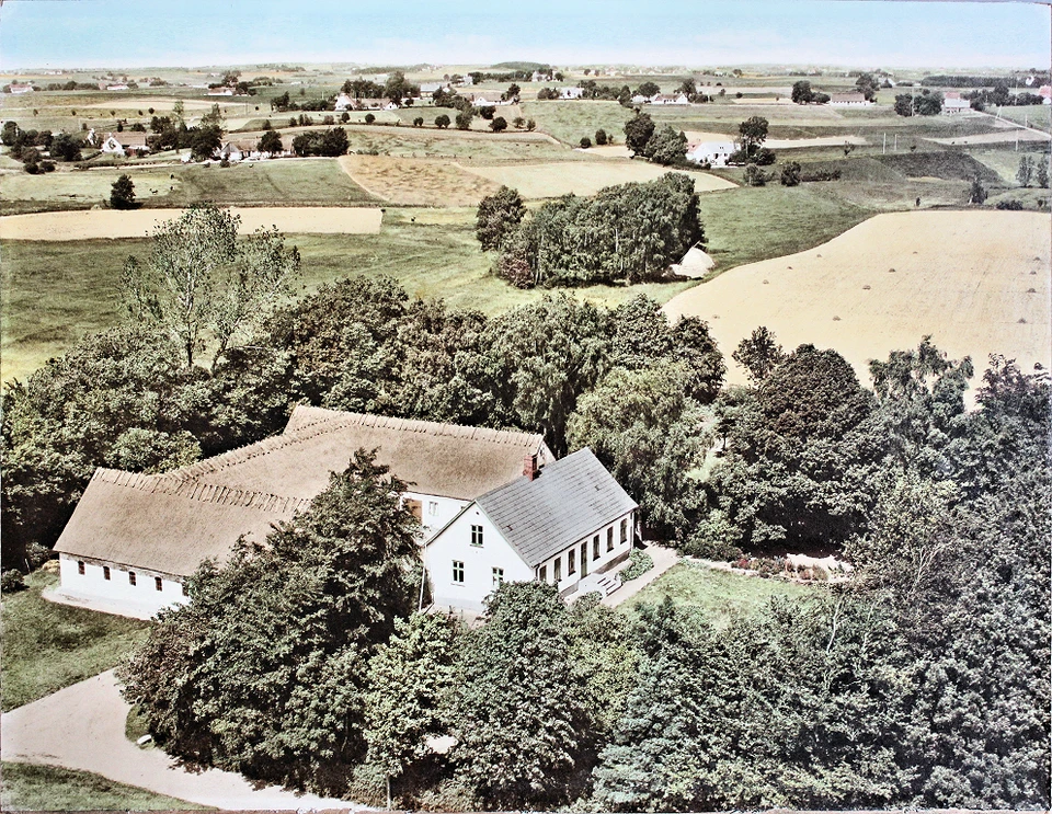 Luftfoto af Bakkegård, Huseby, set mod nord. Luftfoto taget 23. juni 1956. Håndkoloreret af Anna Jensen. Foto af Sylvest Jensen Luftfoto, hvor Anna formentlig arbejdede med at håndkolorere (farvelægge) sorthvide fotografier. Farvefotos indbragte naturligvis firmaet ekstra fortjeneste.