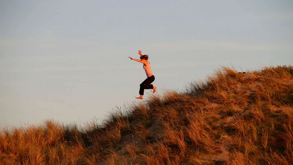 En kvinde i bare tæer, der hopper på en bakke med en blå himmel i baggrunden